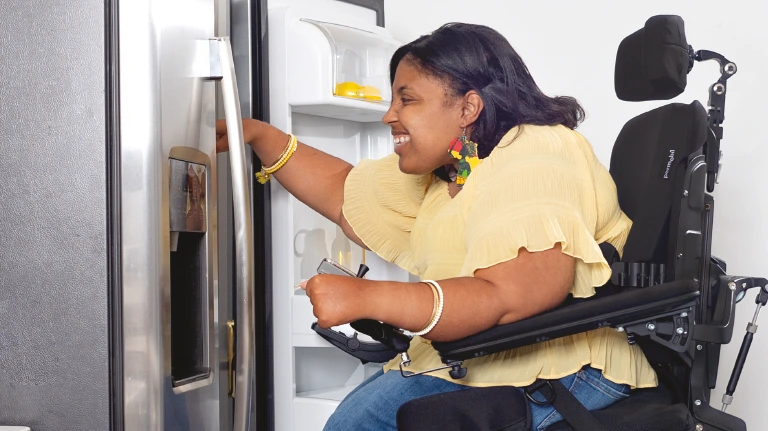 A woman in a Permobil M3 Corpus Powerchair with Active Reach getting something out of the fridge.