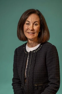 Portrait of Nina Goodheart, tanned woman with dark hair in a bob. Dark blue  textured suit jacket over a white top